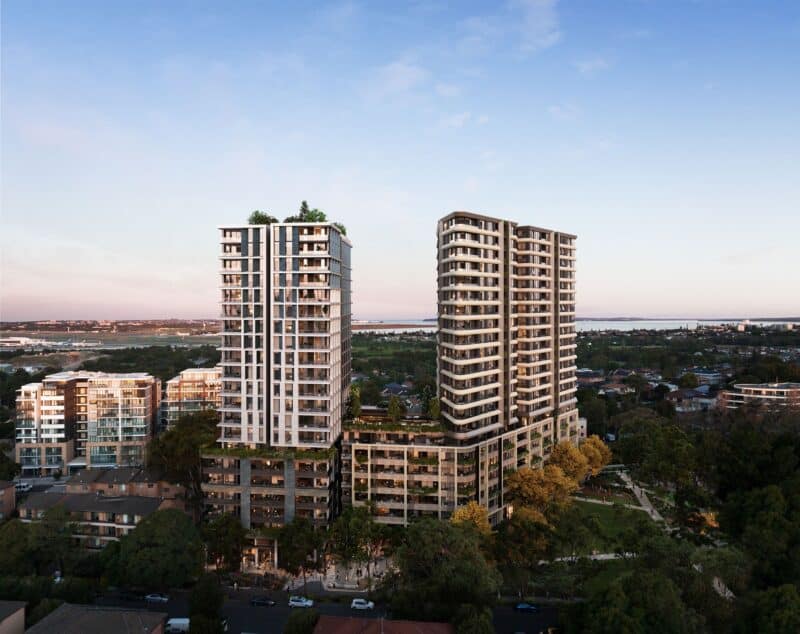Aerial view of modern high-rise apartment buildings in Central Arncliffe, with surrounding trees and a city skyline in the distance, showcasing the vibrant landscape of NSW.