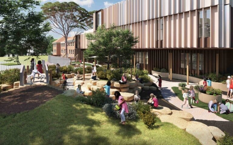 Children play on rocks and grass in a modern school courtyard at Pymble Ladies College, surrounded by trees with a large building in the background, capturing the vibrant spirit of this renowned NSW school.